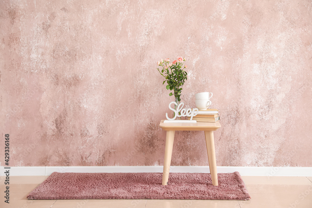 Bedside table with flowers and cups near color wall in room