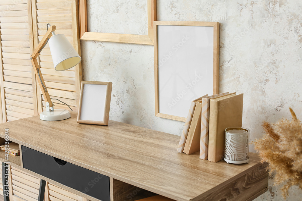 Modern lamp with frame and books on table near light wall