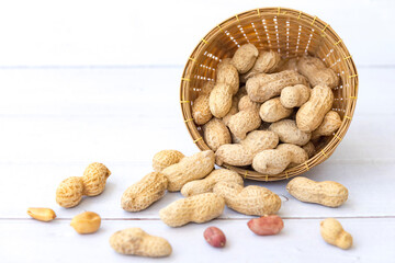 Wall Mural - Peanuts with leaf in wooden basket and peanuts in the peel scattered isolated on wooden white background.Healthy vegetarian concept.