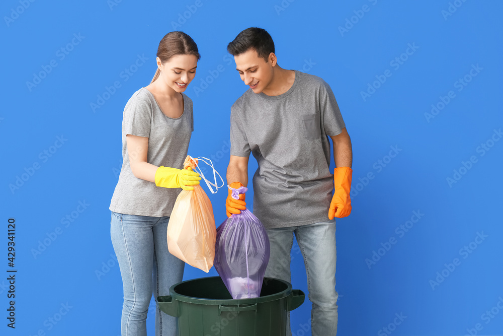 Young couple throwing garbage in trash bin on color background
