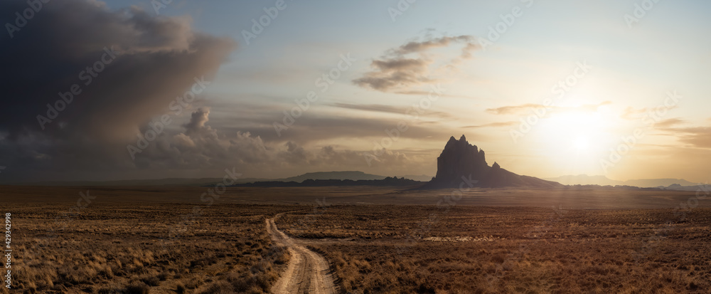 Striking panoramic landscape view of a dirt road in the dry desert with a mountain peak in the background. Colorful Sunset Sky Art Render. Taken at Shiprock, New Mexico, United States. - obrazy, fototapety, plakaty 
