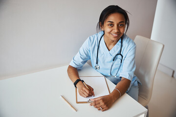 Wall Mural - Beautiful female doctor writing on clipboard in clinic