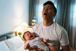 © PR Image Factory - portrait overwhelmed asian father is holding his crying baby daughter and looking upward in despair at midnight in the bedroom at home.