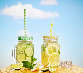 Two Mason jars of Mojito lemonade cocktail with fresh cold ice, lime, lemon and mint leaves