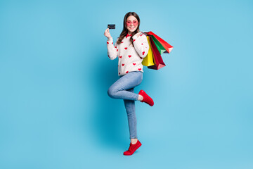 Sticker - Full length photo of young woman dressed hearts print pullover spectacles arms shop bags bank card isolated blue color background