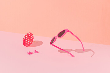 Pink sunglasses, heels and sun umbrella with sunny day shadows against bright pink and peach color background. Minimal summer beach fun concept.