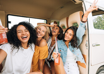 Wall Mural - Four cheerful women enjoying holidays sitting in camper van holding cocktails