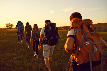 Wall Mural - group of travelers with rucksacks walking in single file in the field during active summer vacation