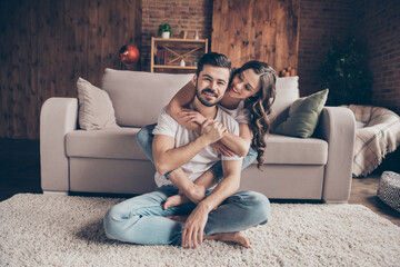 Portrait of attractive careful cheerful couple sitting on floor carpet having fun hugging at loft style interior home house indoor