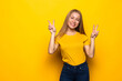 © dianagrytsku - Image of happy young woman standing isolated over yellow background showing peace gesture.