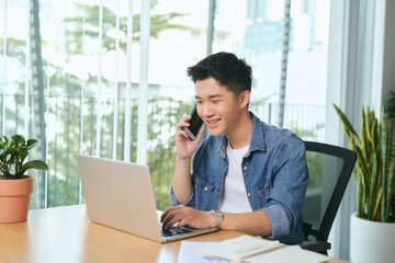 Wall Mural -  man talking on mobile phone, working from home. Portrait of pensive asian businessman using laptop computer, planning project, communication in modern office