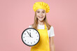 Teen smiling girl chef cook confectioner housewife mother's helper baker in yellow apron white tshirt toque cap hold in hand clock isolated on pastel pink background studio portrait Food cake concept