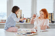 © boytsov - Happy family together: mother and daughter painting together at home using paintbrushes and watercolors. Young woman sitting and helping or teaching daughter sitting on a table to draw