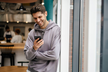 Happy young brunette man holding mobile phone