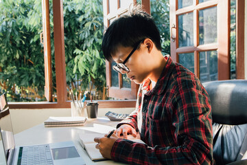 Man hand using a pencil writing notebook paper learning and researching course tutor education, online on technology personal computer laptop Are sitting on the chair people learn and work from home