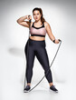 © Romario Ien - Sporty girl with skipping rope. Photo of model with curvy figure in fashionable sportswear on grey background. Sports motivation and healthy lifestyle