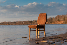 An Empty Soft Old Chair Stands In The Water Next To The Sandy Bank Of The River, Lake. Concept.