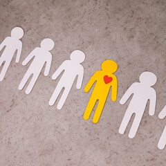 Cut out of white paper figures of people in line. In center is yellow man, with red heart in chest. Falling in love. symbol of meaning of life and human existence.