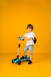 small boy stands with a scooter on a yellow background with space for text. Sports for children