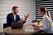 © Drazen - Businessman talking to female coworker while using laptop during a  meeting in the office.