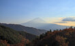 Panoramic view of Mount Fuji from behind a few forested mountains in the late afternoon on a sunny day