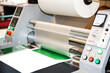 The industrial laminator applies the film to the paper in the production room of the printing house
