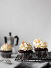 Chocolate cupcakes on a black metal grill on a light background with a coffee pot