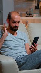 Poster - Caucasian male talking with his collegue about business conference using phone while standing in pajamas on couch. Tired man working late at night in kitchen using modern technology wireless