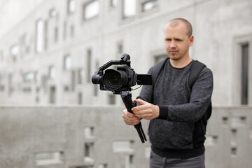 Wall Mural - filmmaking, hobby and creativity concept - videographer shooting video using modern dslr camera on 3-axis gimbal over concrete building. Focus on camera