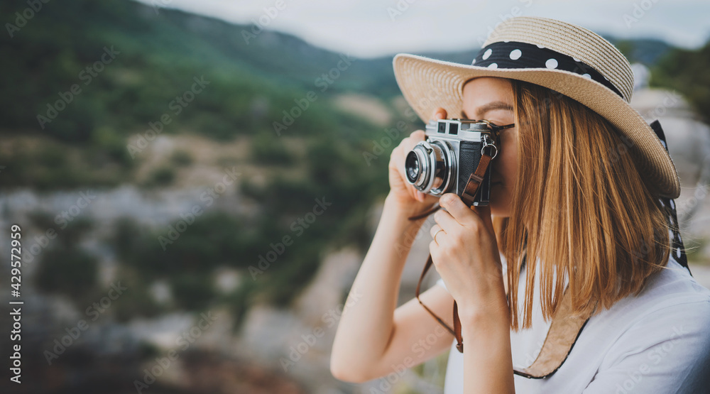 young blonde girl in summer hat takes photo on retro camera on background panorama horizin mountain landscape, hipster tourist enjoys hobby of photographer  leisure in summer nature empty space - obrazy, fototapety, plakaty 
