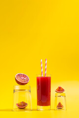 Wall Mural - Red orange juice in glass and oranges on yellow background