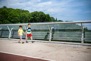 Wall Mural - Portrait of two boys kid a walk over a bridge and looking down, child walking outside in sunny day, Young boys relaxing outdoors in summer on glass bridge. Tourism concept