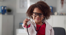 Portrait Of Cute African Child Doctor In White Coat Holding Stethoscope In Clinic Office
