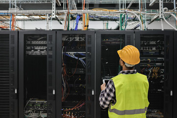 young technician man working with tablet inside big data center room full of rack servers - focus on