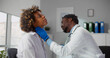 © nimito - African male doctor palpating throat of woman examining female patient during consultation in clinic