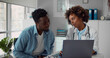 © nimito - Young african woman doctor showing test results to patient on laptop in clinic