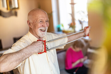 Wall Mural - Senior man exercising using chest expander in living room
