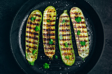 Wall Mural - Grilled zucchini slices in cast iron pan on dark stone or concrete background