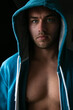 Portrait of handsome young man standing next to window with blue eyes, open hoodie revealing defined pecs