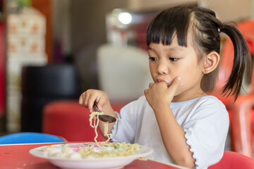 Wall Mural - Portrait​ image​ of​ 2-3 yeas​ old​ of​ baby.​ Happy​ Asian child girl eating and biting the noodle. Enjoy eating moment. Healthy food and kid concept.​ Sucking fingers in the mouth.