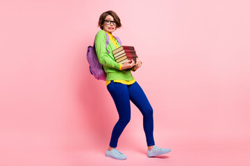 Poster - Full length photo of guilty young lady dressed yellow shirt glasses backpack walking holding book stack isolated pink color background