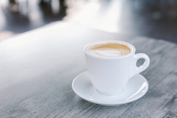 Cup of coffee with latte art on rustic wooden table in a street cafe.