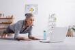 © LIGHTFIELD STUDIOS - middle aged woman doing plank on fitness mat near laptop