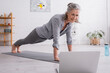 © LIGHTFIELD STUDIOS - happy mature woman practicing and watching yoga tutorial on blurred laptop