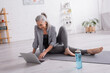 © LIGHTFIELD STUDIOS - smiling mature woman sitting on yoga mat while watching tutorial on laptop