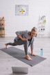 © LIGHTFIELD STUDIOS - happy mature woman with grey hair practicing yoga on mat near sports bottle while watching tutorial on laptop