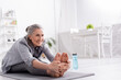 cheerful mature woman with grey hair stretching on yoga mat near sports bottle