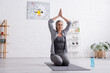 © LIGHTFIELD STUDIOS - mature woman with grey hair and praying hands above head practicing yoga near sports bottle