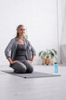 © LIGHTFIELD STUDIOS - happy mature woman with grey hair practicing yoga near sports bottle