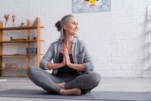 Happy Mature Woman With Grey Hair Sitting With Praying Hands In Lotus Pose On Yoga Mat